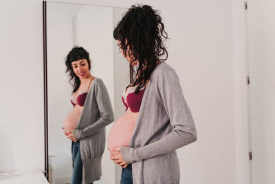 Pregnant smiling young woman standing in front of mirror