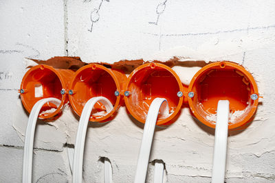 Orange, round junction box mounted in the white wall with protruding electric cables.