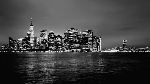 Illuminated buildings by sea against sky in city at night