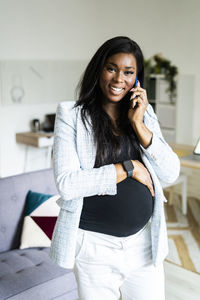 Happy pregnant businesswoman talking on smart phone while standing with hand on stomach