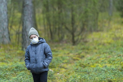 Girl wearing hooded jacket and mask standing in forest