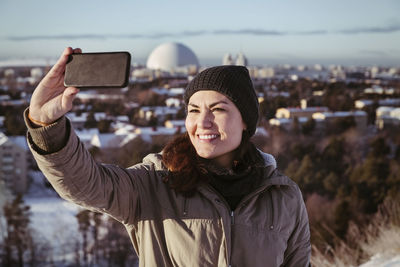 Smiling woman clicking selfie through smart phone during winter