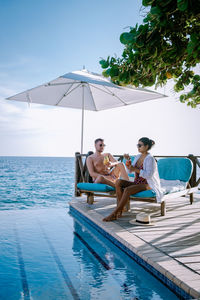 Couple sitting by swimming pool against sky