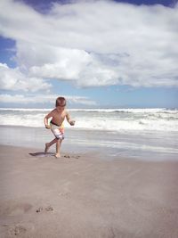 Shirtless boy playing on shore at beach against sky