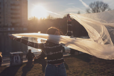 Woman holding textile while standing on field against sky