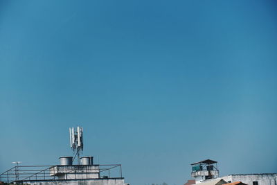 Low angle view of communications tower on building against blue sky