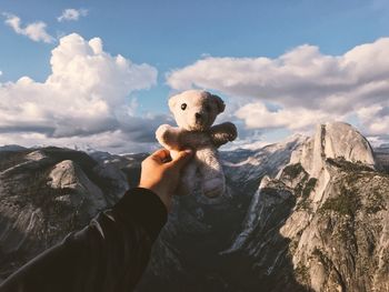 Cropped hand of person holding teddy bear over mountains at yosemite national park