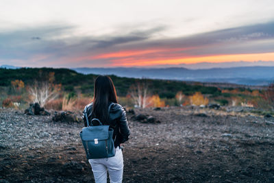 Rear view of woman standing on field against sky during sunset