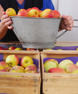 Midsection of woman holding apples in container at market