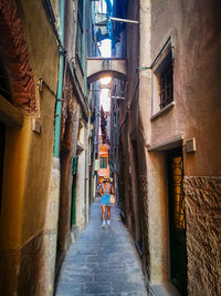 Rear view of woman walking on narrow alley amidst buildings