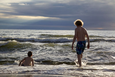 Rear view of boys on beach against sky