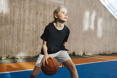 Pre-adolescent girl looking away while playing basketball at sports court