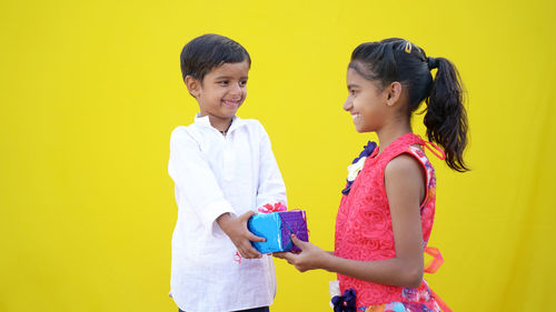 Side view of friends using smart phone while standing against yellow background