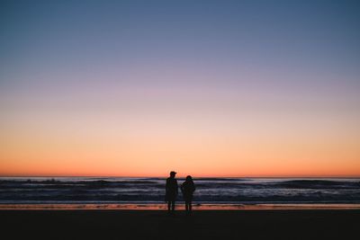 Silhouette couple standing on beach against clear sky during sunset