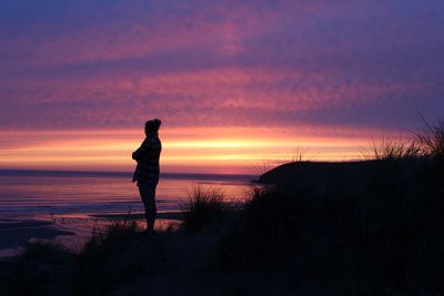 Silhouette woman standing on beach against sky during sunset