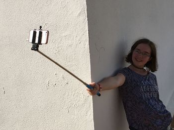 Smiling teenage girl taking selfie by wall