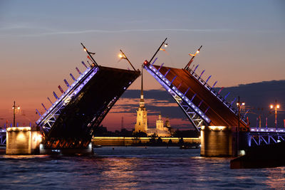 Cranes by river against sky at night