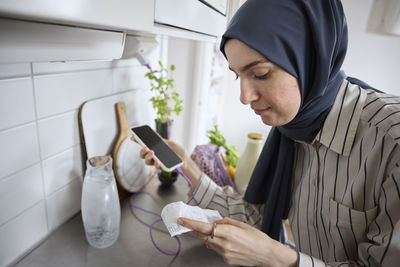 Woman in headscarf unpacking groceries at home and checking receipt