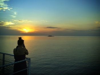 Rear view of silhouette man sitting on shore against sunset sky