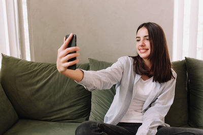 Young woman using phone while sitting on sofa