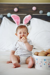 Portrait of baby girl crying with eggs sitting on bed at home