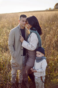 Family of three with a boy child mom and dad are standing on field in autumn at sunset