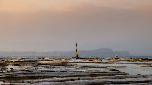 Statue of lighthouse at seaside during sunset