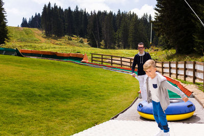 Boy pulling inflatable ring with father on footpath against trees