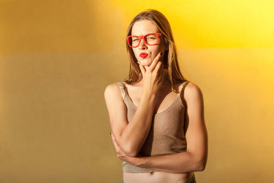 Portrait of beautiful young woman standing against yellow wall