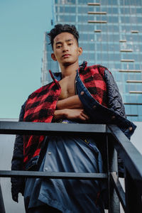 Low angle view portrait of young man standing by railing against building