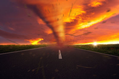 Road amidst field against dramatic sky during sunset