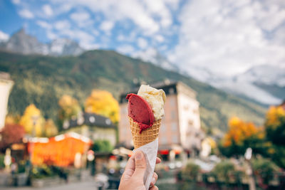 Cropped hand holding ice cream cone against sky