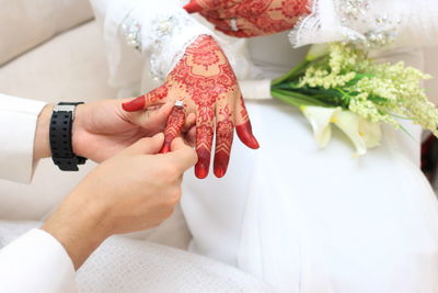 Midsection of groom putting ring in bride finger sitting on sofa during wedding