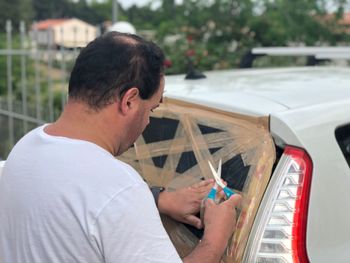 Man fixing broken rear windshield of car with tape