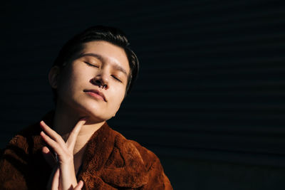 Woman with eyes closed standing against black background