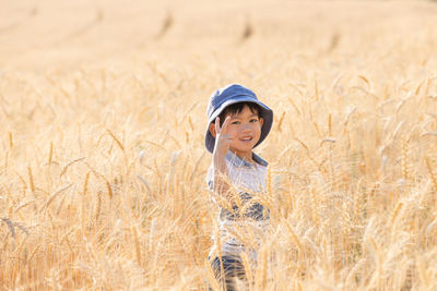 Portrait of boy gesturing while standing by plants in agricultural field