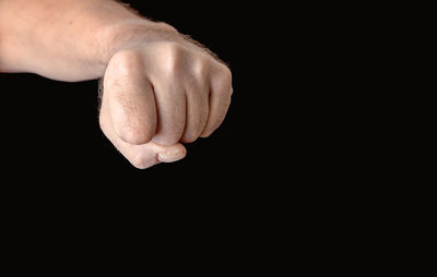 Cropped hand of man showing fist against black background