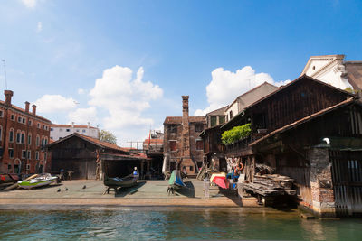 People on canal amidst buildings in city against sky