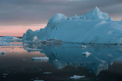 Iceberg in sea against cloudy sky during sunset