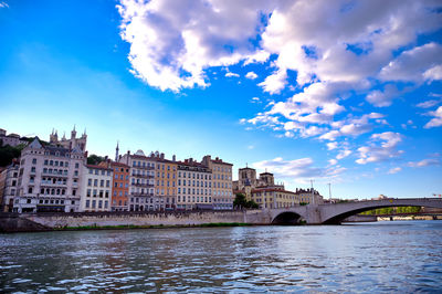 Buildings by river against blue sky