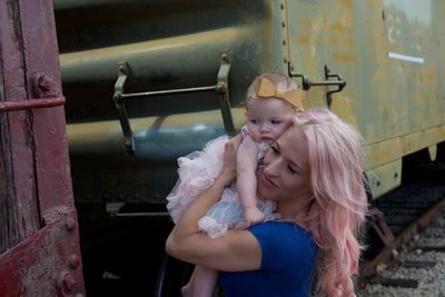 Woman carrying daughter while standing by train