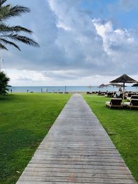 Footpath leading towards sea against sky