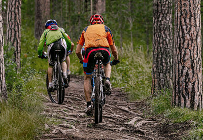Back group cyclists riding mountain bike. uphill on muddy trail with roots