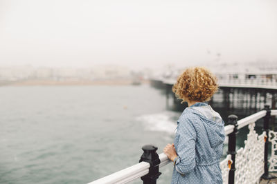 Rear view of young woman standing by railing on brighton pier