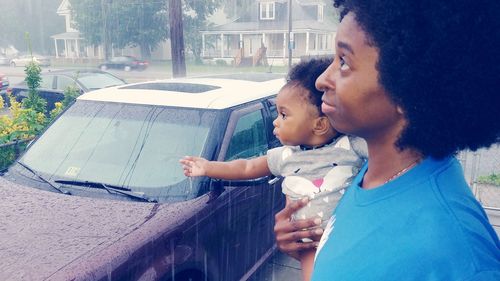 Side view of mother carrying daughter while standing outdoors during rainfall