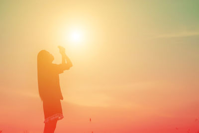 Silhouette woman photographing orange sky during sunset