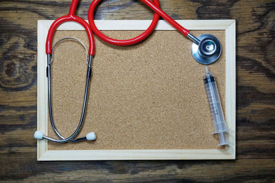 High angle view of picture frame with syringe and stethoscope on wooden table