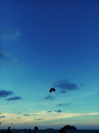 Silhouette of person paragliding against blue sky