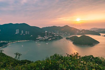 High angle view of sea and cityscape against sky at sunset