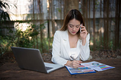 Young woman talking on mobile phone while working at table